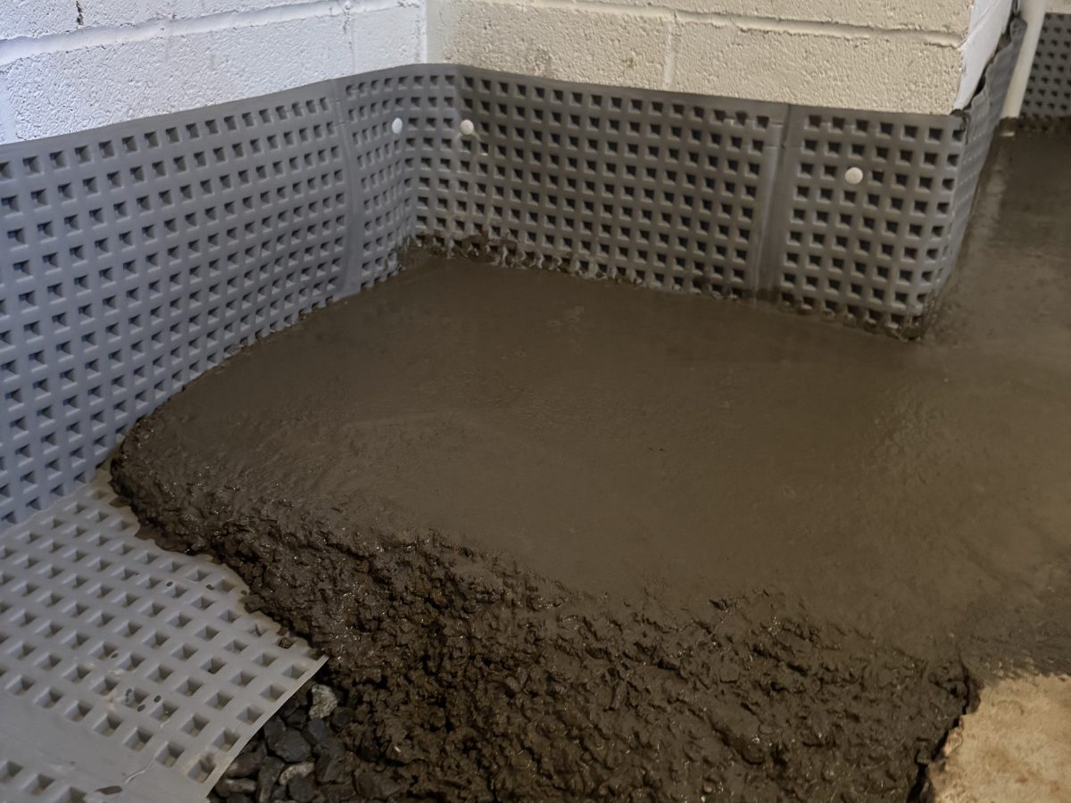 Interior perimeter drain trench freshly repoured with concrete along a basement wall