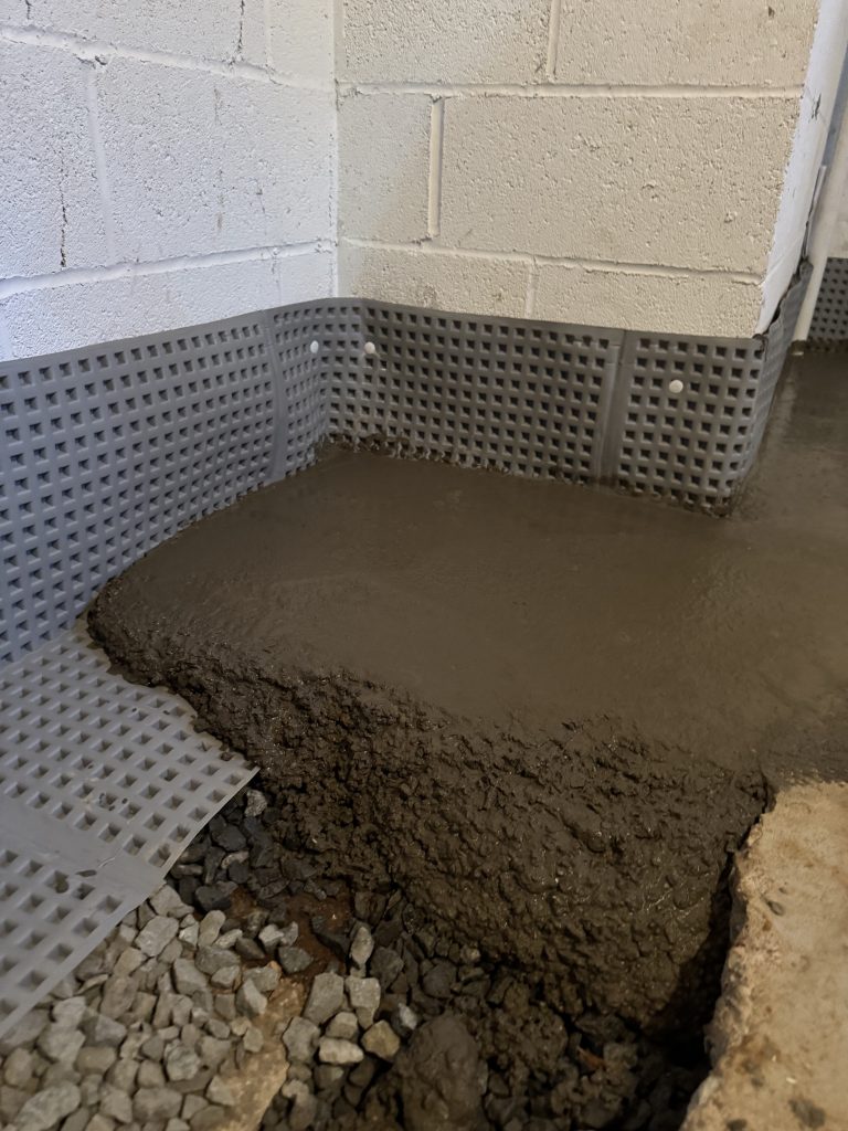 Interior perimeter drain trench freshly repoured with concrete along a basement wall